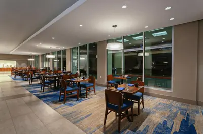 a dining room with tables and chairs and windows at Holiday Inn Los Angeles - LAX Airport by IHG in Los Angeles