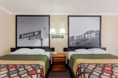 two beds in a hotel room with posters on the walls at Super 8 by Wyndham Los Angeles Downtown in Los Angeles