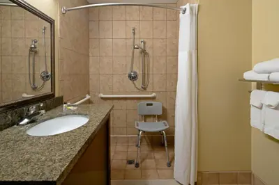 a bathroom with a sink and a shower and a chair at Staybridge Suites Palmdale by IHG in Palmdale