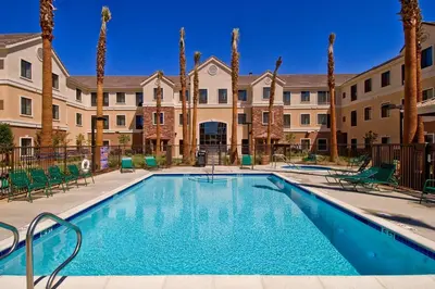 a swimming pool with palm trees and buildings at Staybridge Suites Palmdale by IHG in Palmdale