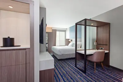 a hotel room with a bed and a desk with a mirror at SpringHill Suites by Marriott Huntington Beach Orange County in Huntington Beach