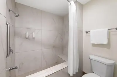 a white bathroom with a shower and a toilet at Travelodge Inn & Suites by Wyndham Anaheim on Disneyland Dr in Anaheim