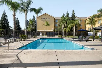 a swimming pool in front of a hotel with palm trees at Homewood Suites Bakersfield in Bakersfield