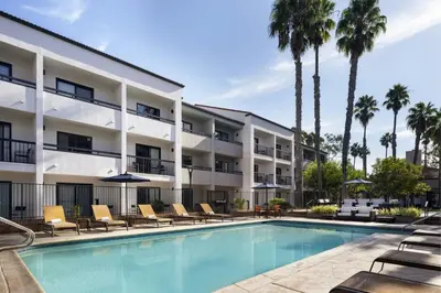 a hotel with a swimming pool with chairs and palm trees at Courtyard Los Angeles Torrance/Palos Verdes in Torrance