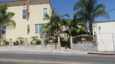 a building with a fence and palm trees in front of it at Trylon Hotel - Hollywood in Los Angeles
