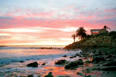 a beach with palm trees and a pier at sunset at Cliff House Inn in Carpinteria