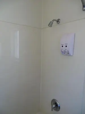 a bathroom with a shower with a soap dispenser at American Inn in Ontario