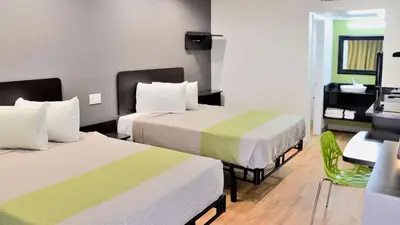 a hotel room with two beds and a green chair at Studio 6-Buttonwillow, CA in Buttonwillow