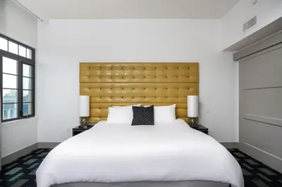 a bedroom with a large white bed with a yellow headboard at Padre Hotel in Bakersfield