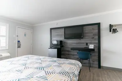 a bedroom with a bed and a desk with a television on a wall at Motel 6 Pico Rivera - Los Angeles, CA in Pico Rivera