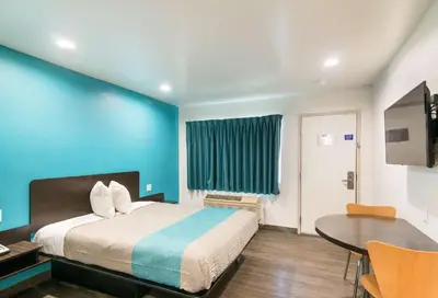 a bedroom with a bed and a table and a blue wall at Motel 6-South El Monte, CA - Los Angeles in South El Monte