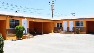 a yellow building with doors and stairs in a parking lot at Aristocrat Motel in Baldwin Park