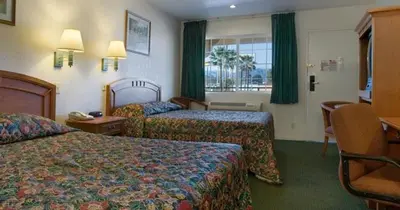 a hotel room with two beds with green curtains at Orange Show Inn in San Bernardino