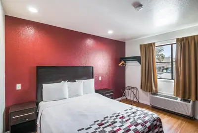 a hotel room with a bed and a red wall at Red Roof Inn Palmdale - Lancaster in Palmdale