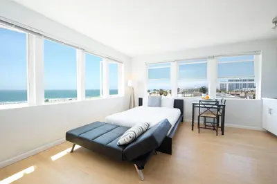 a bedroom with a bed and a table and windows at AIR Venice on the Beach in Los Angeles