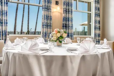 a table with a white table cloth and a vase of flowers at Jamaica Bay Inn Marina Del Rey Tapestry Collection by Hilton in Los Angeles