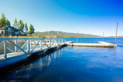 a dock on a lake with a house in the background at Little Pines Couples Lakeside Cabin by Big Bear Vacations in Big Bear Lake