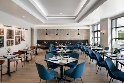 a dining room with tables and blue chairs at Sheraton Cerritos in Buena Park