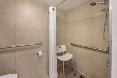 a bathroom with a shower with a toilet and a chair at City Express by Marriott Manhattan Beach in Manhattan Beach