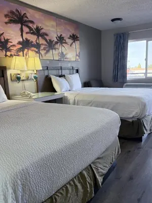 two beds in a hotel room with palm trees on the wall at Days Inn by Wyndham Ontario Airport in Ontario