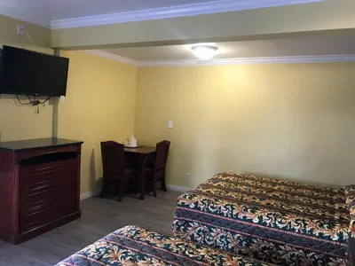 a hotel room with two beds and a desk with a television at Colony Inn Motel in Bellflower