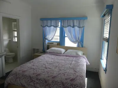 a bedroom with a bed with a purple comforter and a window at Hotel del Flores in Los Angeles