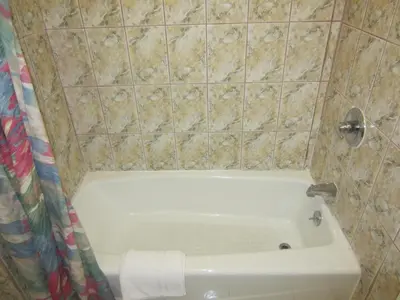 a bathroom with a white tub and a tiled wall at Travel Eagle Inn Motel in Long Beach