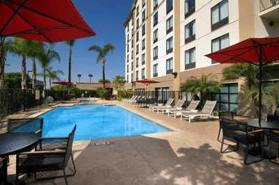 a pool with chairs tables and umbrellas next to a hotel at Hampton Inn & Suites Anaheim Garden Grove in Anaheim