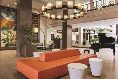a living room with an orange couch and a piano at Embassy Suites by Hilton Brea - North Orange County in Brea