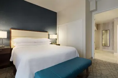 a bedroom with a large white bed and a blue bench at Embassy Suites by Hilton Brea - North Orange County in Brea