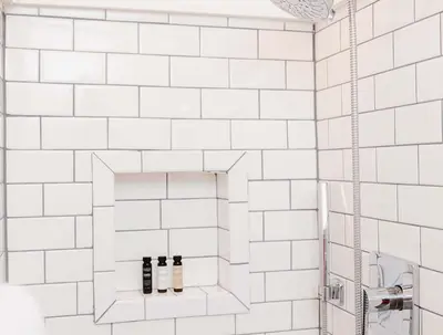 a white tiled shower with three bottles on a shelf at Grand Pine Cabins in Wrightwood