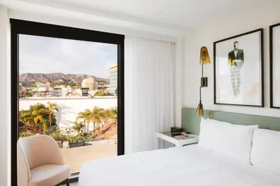 a bedroom with a bed and a chair and a window at The Godfrey Hotel Hollywood in Los Angeles