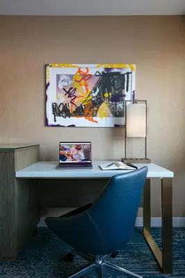 a desk with a blue chair and a painting on the wall at Hotel Dena, Pasadena Los Angeles, a Tribute Portfolio Hotel in Pasadena