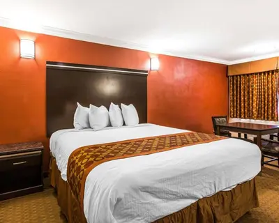 a hotel room with a large bed with orange walls at Rodeway Inn & Suites Corona in Corona