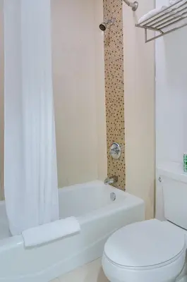 a white bathroom with a toilet and a bath tub at Eden Roc Inn & Suites near the Maingate in Anaheim