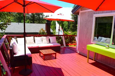 a deck with red umbrellas and a couch and a table at Dream Getaway-Secluded Hot Spa-Walk to Village-Walk to Pineknot Trailhead-Plus King Bed! in Big Bear Lake