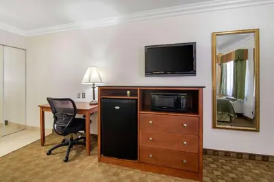 a hotel room with a desk and a television on a wall at Rodeway Inn Adelanto US 395 in Adelanto