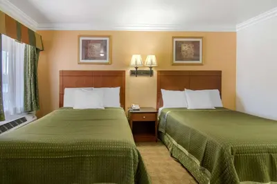 two beds in a hotel room with green sheets at Rodeway Inn Adelanto US 395 in Adelanto