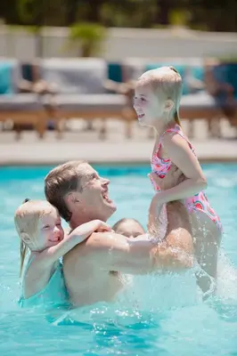 a man holding two children in a swimming pool at Anaheim Resort Suites in Anaheim