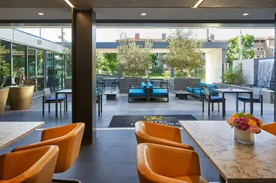 a restaurant with orange chairs and tables and windows at Hotel Mariposa in Los Angeles