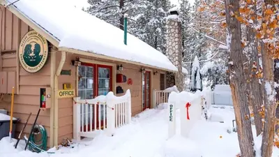 a house covered in snow with a fence in front at Sleepy Forest Cottages in Big Bear Lake