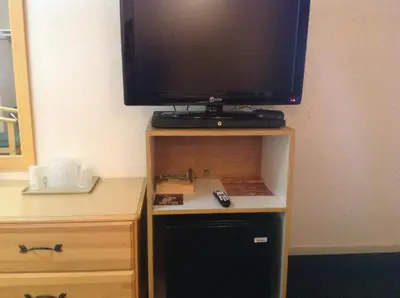 a television on top of a wooden stand with a black refrigerator at Beach Inn in Long Beach
