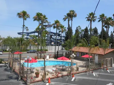 a pool with red umbrellas and a roller coaster at Best Inn & Suites in Anaheim