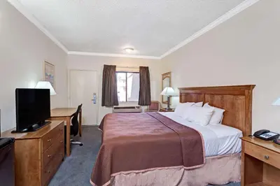 a hotel room with a bed and a desk and a television at Travelodge by Wyndham Pasadena Central in Pasadena