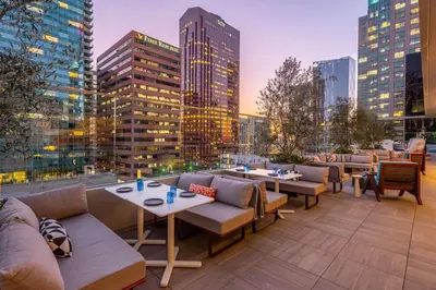 a rooftop patio with tables and chairs and a city skyline at The Wayfarer Downtown LA, Tapestry Collection by Hilton in Los Angeles