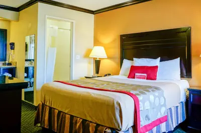 a hotel room with a large bed with a red pillow at Ramada by Wyndham Ontario Airport & Convention Center in Ontario