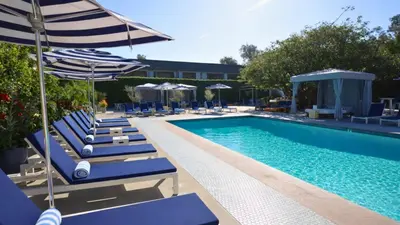 a pool with blue lounge chairs and umbrellas next to it at Luxe Sunset Boulevard Hotel in Los Angeles