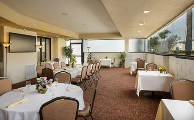a dining room with white tables and chairs at Coast Burbank Hotel in Burbank