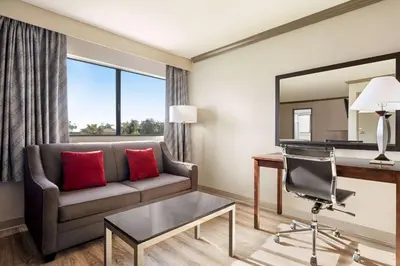 a living room with a couch and a desk and a mirror at Baymont by Wyndham Monterey Park in Monterey Park