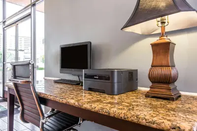 a desk with a computer and a monitor and a lamp at Quality Inn & Suites Bell Gardens-Los Angeles in Bell Gardens